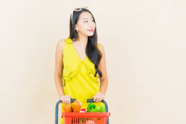 Renkli arka planda süpermarketten alınmış market sepetiyle gülümseyen güzel Asyalı kadın portresi.
