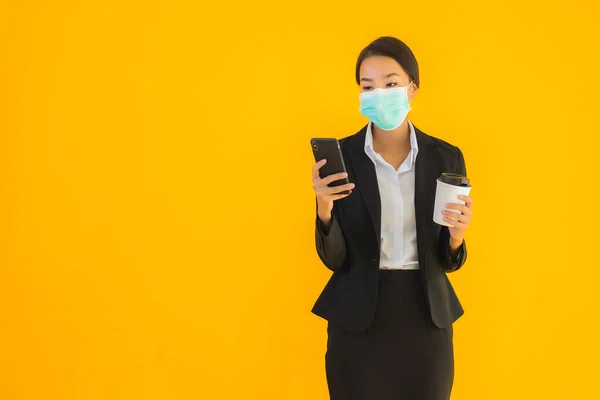 肖像画美しい若いビジネスアジアの女性は 黄色の隔離された背景にCovid19とコロナウイルスの概念のためのコーヒーと携帯電話を使用マスクを着用 — ストック写真
