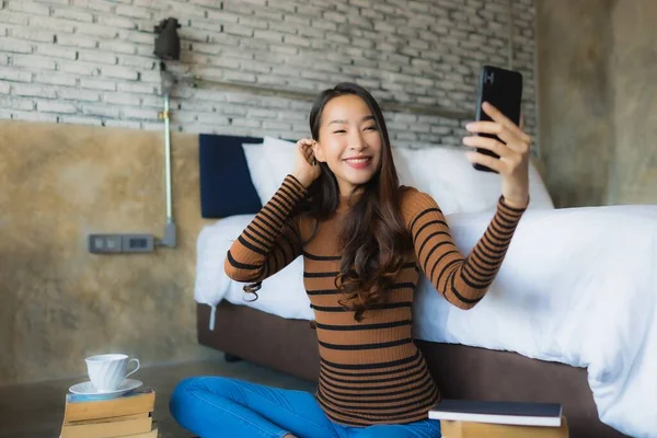 年轻的亚洲女人在卧室里使用带有读书机和咖啡杯的智能手机 — 图库照片