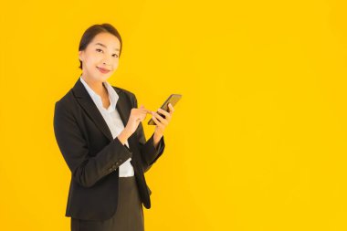 Portre güzel genç Asyalı kadın akıllı cep telefonu ve kahve fincanı ile izole edilmiş sarı arka planda