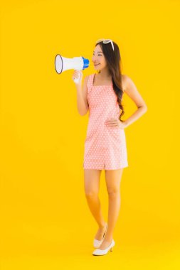 Güzel bir Asyalı kadın, sarı izole edilmiş arka planda megafonla yüksek sesle konuşur.