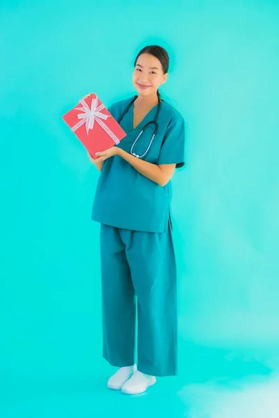 美丽的年轻亚洲医生女性在蓝色孤立的背景下展示红色礼品盒 — 图库照片