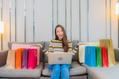 Asyalı güzel bir kadının portresi kanepeye dizüstü bilgisayar kullanıyor.