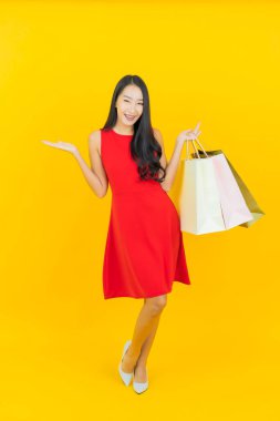 Sarı arka planda alışveriş çantasıyla gülümseyen güzel Asyalı kadın portresi