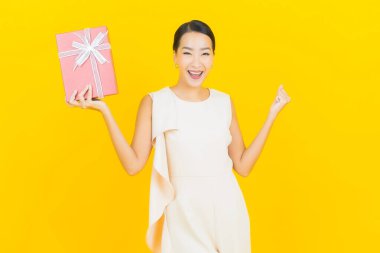 Asyalı güzel bir kadının portresi. Sarı arka planda kırmızı hediye kutusuyla gülümsüyor.