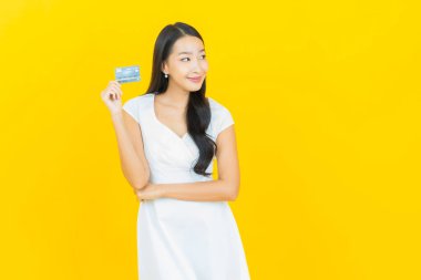Asyalı güzel bir kadının portresi. Sarı arka planda kredi kartıyla gülümsüyor.