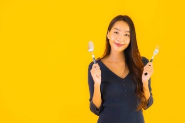 Güzel, genç Asyalı bir kadının portresi. Kaşığı ve çatalı ile sarı izole edilmiş arka planda yemeye hazır.