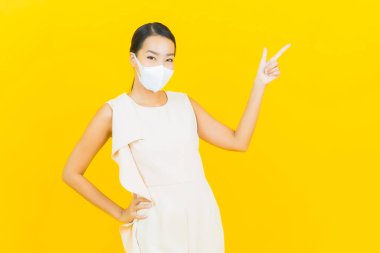 Sarı arka planda Covid19 veya virüsü korumak için maskeli güzel Asyalı kadın portresi