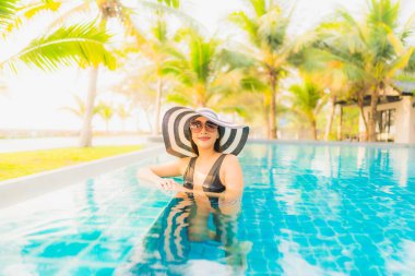 Güzel bir Asyalı kadın portresi, gün batımında palmiye ağacıyla birlikte havuz kenarında dinleniyor ya da tatil için gün doğumunda dinleniyor.