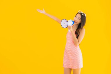 Güzel bir Asyalı kadın, sarı izole edilmiş arka planda megafonla yüksek sesle konuşur.