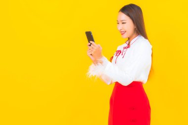 Sarı arka planda akıllı cep telefonlu güzel Asyalı kadın portresi.