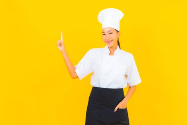 Güzel bir Asyalı kadın portresi ya da sarı izole arkaplanda şapkası olan aşçı üniforması.