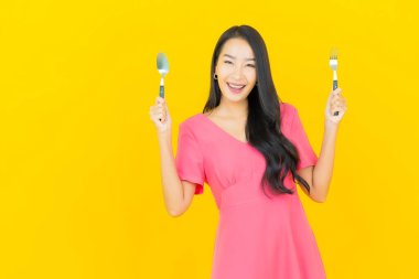 Asyalı güzel bir kadının portresi sarı arka planda çatal ve kaşıkla gülümsüyor.