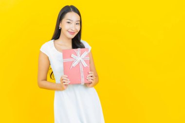 Asyalı güzel bir kadının portresi. Sarı arka planda kırmızı hediye kutusuyla gülümsüyor.