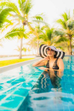 Güzel bir Asyalı kadın portresi, gün batımında palmiye ağacıyla birlikte havuz kenarında dinleniyor ya da tatil için gün doğumunda dinleniyor.