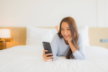 Güzel bir Asyalı kadın yatak odasının içinde akıllı cep telefonu kullanıyor.