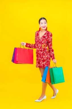 Sarı arka planda renkli alışveriş çantalı güzel Asyalı kadın portresi.