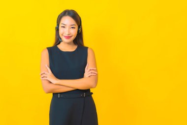 Sarı arka planda kulaklık takmış güzel Asyalı iş kadını portresi.