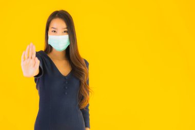 Koronavirüsten korunmak için maske takmış güzel Asyalı bir kadın portresi ve sarı izole edilmiş arka planda 19 numara.