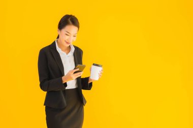 Portre güzel genç Asyalı kadın akıllı cep telefonu ve kahve fincanı ile izole edilmiş sarı arka planda