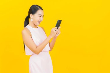 Asyalı güzel bir kadının portresi sarı arka planda akıllı cep telefonuyla gülümsüyor.