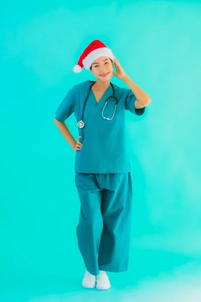 Portrait beautiful young asian doctor woman wear christmas hat with smile happy on blue isolated background
