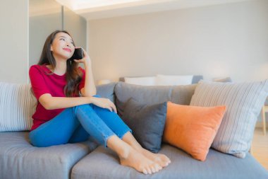 Güzel bir Asyalı kadın portresi. Yatak odasının iç tarafındaki oturma odasındaki koltukta akıllı cep telefonu kullanıyor.