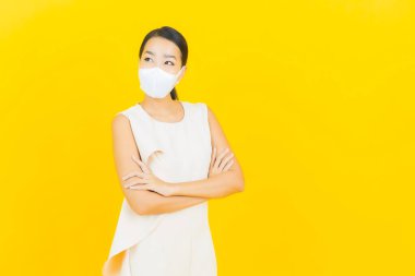 Sarı arka planda Covid19 veya virüsü korumak için maskeli güzel Asyalı kadın portresi