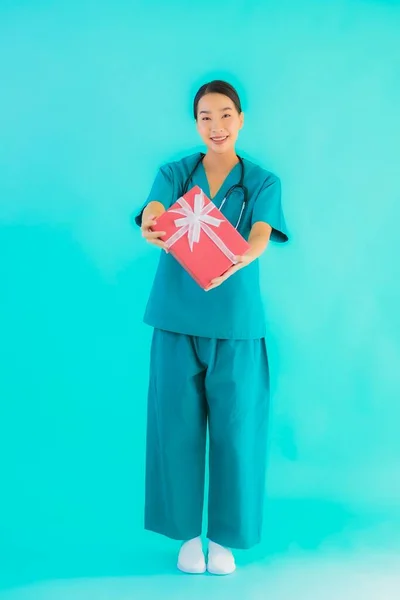 Portrait beautiful young asian doctor woman show red gift box on blue isolated background