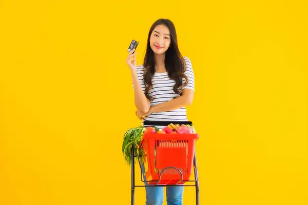 肖像画美しい若いアジアの女性ショッピングスーパーマーケットからクレジットカードで黄色の隔離された背景 — ストック写真