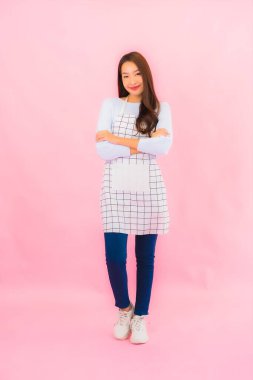 Portrait beautiful young asian woman in kitchen wear with apron on pink isolated background