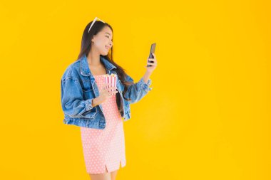 Güzel bir Asyalı kadın portresi telefon patlamış mısırı ve sarı izole edilmiş bir arka planda film izlemekten memnun.