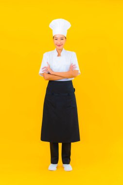 Güzel bir Asyalı kadın portresi ya da sarı izole arkaplanda şapkası olan aşçı üniforması.