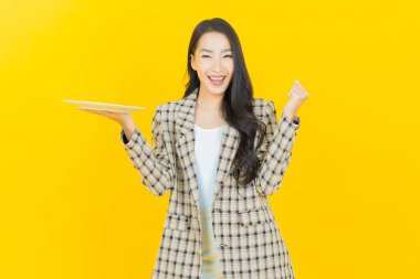 Güzel Asyalı bir kadının portresi. Arka planda boş tabak tabağıyla gülümsüyor.