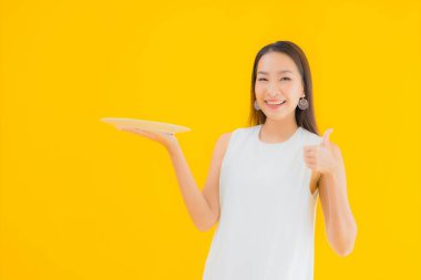 Güzel bir Asyalı kadın portresi boş tabak ve tabakla izole edilmiş sarı arka planda.