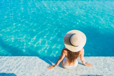 Asyalı güzel bir kadının portresi gülümsüyor şehir manzaralı açık havuz etrafında rahatça yüzüyor.