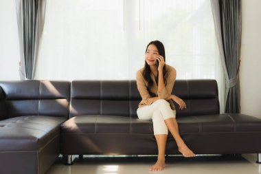 Güzel bir Asyalı kadın portresi. Kanepenin iç tarafında cep telefonu ya da kahve fincanı ile cep telefonu kullanıyor.