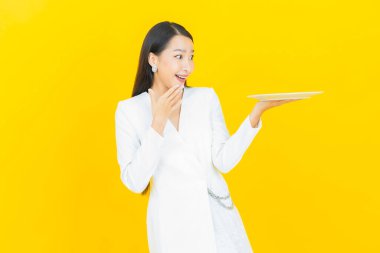 Güzel Asyalı bir kadının portresi. Arka planda boş tabak tabağıyla gülümsüyor.