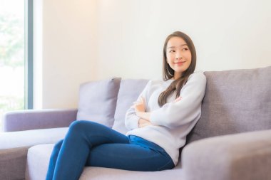 Portre güzel genç Asyalı kadın rahatla kanepede gülümse oturma odasında
