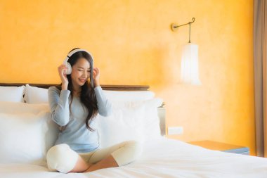 Asyalı güzel bir kadının portresi. Yatak odasının içinde müzik dinlemek için cep telefonu ve kulaklık kullanıyor.