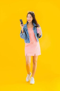 Güzel bir Asyalı kadın portresi telefon patlamış mısırı ve sarı izole edilmiş bir arka planda film izlemekten memnun.