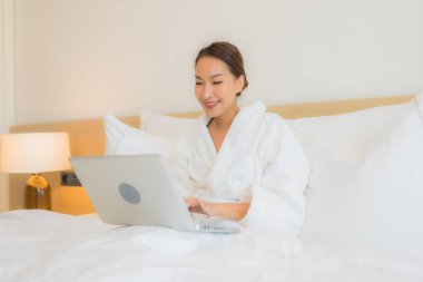 Güzel bir Asyalı kadın yatak odasının iç kısmında bilgisayar kullanıyor.