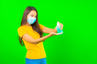 Güzel Asyalı genç bir kadının portresi, yeşil yalıtılmış arka planda kovid19 veya koronavirüsten korunmak için maske takar.