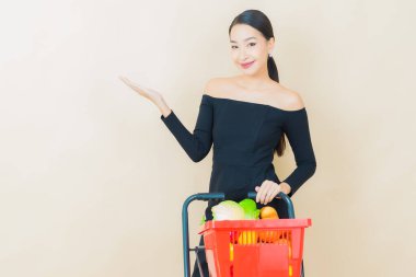 Renkli arka planda süpermarketten alınmış market sepetiyle gülümseyen güzel Asyalı kadın portresi.