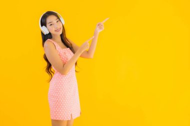 Güzel bir Asyalı kadın portresi. Sarı izole edilmiş arka planda akıllı cep telefonu ve kulaklıkla müzik dinliyor.