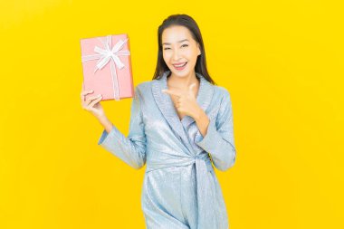 Asyalı güzel bir kadının portresi. Sarı arka planda kırmızı hediye kutusuyla gülümsüyor.