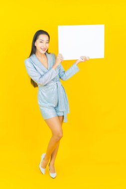 Asyalı güzel bir kadının portresi. Sarı arka planda boş beyaz ilan panosuyla gülümsüyor.