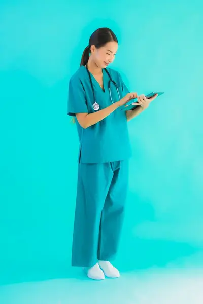 Portrait beautiful young asian doctor woman use smart tablet device on blue isolated background