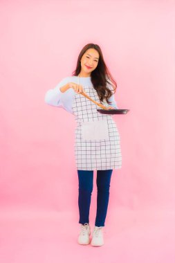 Portrait beautiful young asian woman in kitchen wear with apron on pink isolated background