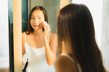 Güzel bir Asyalı kadın portresi. Yüzünü ve yüzünü banyo içinde aynayla temizliyor.